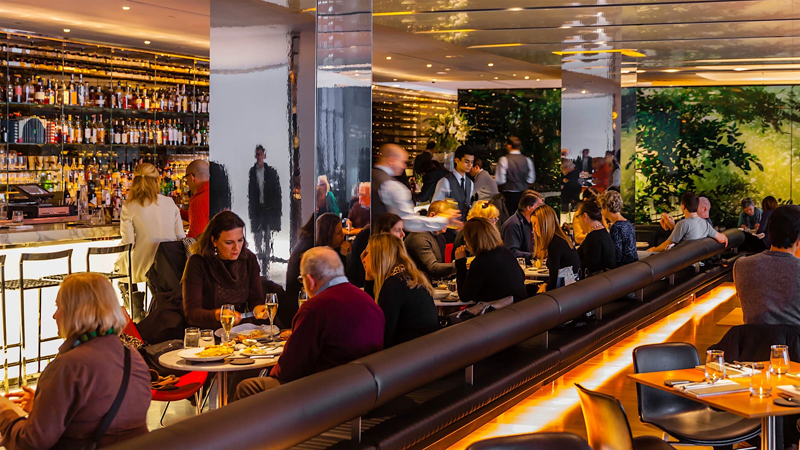 The bar area of the Modern, where guests dine amidst mirrored columns, a bright bar, leather chairs and tree-like designs on the wall